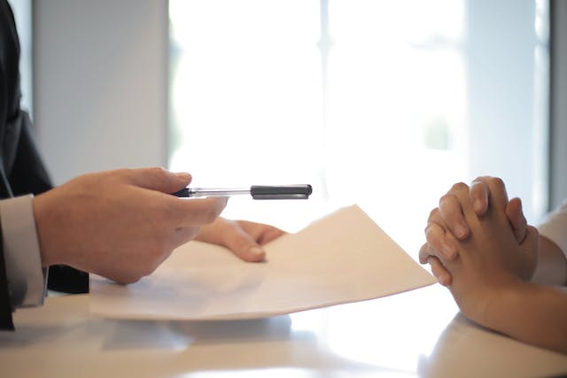 Person Handing Over Paper and Pen